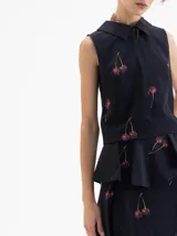 Top sin mangas color azul marino con cuello camisero y peplum en la cintura. Presenta un estampado de cerezas.