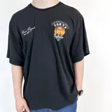 Remera negra de algodón de corte oversize, con estampado en el frente de la ciudad de Tokio al atardecer y texto en blanco y naranja.