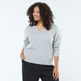 Sweater de punto gris con cuello en V, mangas largas y puños acanalados.