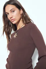 Top de punto acanalado color marrón, de manga larga y calce ajustado al cuerpo. Presenta escote redondo y detalle de botones en los puños.