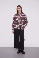 Campera tipo camisa de manga larga con cierre frontal de botones metálicos, bolsillos frontales con solapa y diseño estampado tipo tie-dye en tonos marrones y blancos.