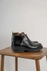 Botinetas negras con suela track, combinando cuero texturizado en la parte frontal y cuero charolado en la parte trasera. Diseño de caña baja con detalle de corte lateral.