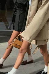 Trench color beige con cuello de solapa subido y manga larga. Tiene bolsillos laterales, forro interior y cinturón de lazo en el mismo tejido. El cuello se cierra con un botón.