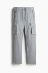 Pantalón cargo de nylon color gris claro, con cintura elástica y cordón ajustable. Presenta bolsillos laterales con cierre, bolsillos cargo con solapa en las piernas y cordón ajustable en los bajos.
