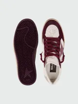 Zapatillas de estilo urbano con diseño desgastado, combinan paneles de cuero blanco y gamuza en color bordó. Presentan una estrella lateral con acabado brillante, cordones al tono y suela de goma con efecto envejecido.