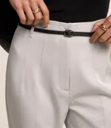 Pantalón zanahoria de vestir color gris claro, con cintura alta, cinturón con hebilla metálica y corte holgado en las caderas que se estrecha en las piernas.