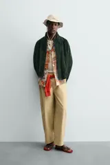Cazadora regular fit de piel con acabado en ante color verde oscuro, de la colección especial Gabriel Azevedo x ZARA. Cuenta con cuello subido, manga larga, bolsillos de vivo en la cadera, bolsillo interior y bajo acabado con elástico. Cierre frontal con cremallera oculta por solapa con botones a presión.