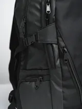 Mochila negra con múltiples bolsillos con cierre, correas ajustables y logo de la marca en el frente.