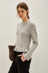 Sweater de punto color gris melange, con cuello redondo, manga larga y detalle de volado en el ruedo. Presenta pequeñas aplicaciones de strass distribuidas por toda la prenda.