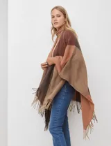 Ruana tejida con diseño colorblock en tonos de gris y beige, con flecos en el borde inferior.