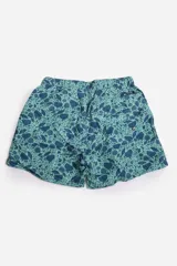 Short de baño celeste con estampado de hojas pequeñas en tonos verdes y blancos. Cuenta con cintura elástica con cordón ajustable, bolsillos laterales y un parche circular con logo en la parte inferior.