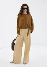 Pantalón recto de tiro medio color beige, confeccionado en mezcla de lino y viscosa. Cuenta con detalle de pinzas, bolsillos laterales y cierre frontal oculto con cremallera, botón y ganchos con tapeta.