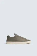 Zapatilla de estilo urbano confeccionada en piel con acabado de serraje, diseño minimalista con cordonera oculta y suela de goma a contraste.