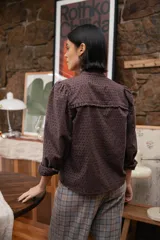 Camisa de broderie color chocolate, con cuello alto con volados, cierre frontal de botones y mangas largas con volumen.