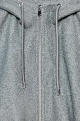 Chaqueta estilo bomber de corte oversize en color marrón oscuro, confeccionada en tejido suave. Presenta capucha con cordones ajustables, cierre frontal con cremallera, mangas largas con puños elásticos y bolsillos delanteros de vivo. El bajo cuenta con detalle de pliegues.
