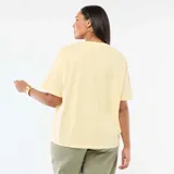 Remera de corte oversize en color amarillo claro, con cuello redondo y mangas cortas. Presenta un estampado gráfico frontal con la frase 'COSTA AZUL' en letras verdes y un diseño de sol, acompañado por el texto 'Palma de Majorque' en tipografía cursiva.