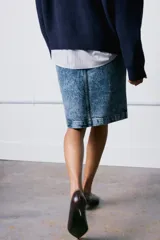 Falda midi de tiro medio confeccionada en denim con efecto lavado. Presenta cintura con trabillas, cierre frontal con cremallera, botón y gancho metálico, y una abertura en el bajo.