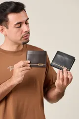 Billetera de cuero sintético con acabado liso, diseño plegable y detalle metálico decorativo en la parte frontal.