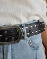 Cinturón de cuero marrón oscuro con tachas metálicas redondas en tonos bronce, plata y dorado. Hebilla rectangular de metal con acabado envejecido.