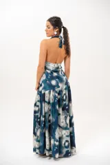 Vestido largo con escote halter profundo y diseño sin mangas. Presenta un estampado difuminado en tonos azules, celestes, blancos y grises, con corte ajustado en el torso y una falda larga con vuelo.