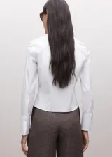 Camisa blanca de algodón, de corte clásico con cuello camisero, manga larga y cierre frontal con botones.