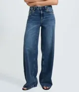 Pantalón wide leg de jeans azul oscuro, con cintura media y detalle de tachuelas metálicas a lo largo de las costuras laterales. Cuenta con bolsillos funcionales, trabillas para cinturón y cierre frontal con botón y cremallera.