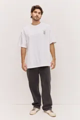 Remera oversize blanca de manga corta, con cuello redondo y diseño holgado. Presenta una pequeña estampa gráfica a la altura del pecho.
