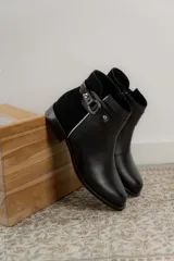 Botas cortas de cuero negro con paneles traseros de gamuza, cierre lateral y detalle de correa con hebilla metálica en el tobillo.