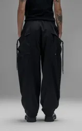 Pantalón de estilo utilitario y corte oversize, confeccionado en textil técnico liviano. Presenta cintura elástica con cordón ajustable, bolsillos laterales envolventes de gran tamaño con cordones y tancas de ajuste, y elásticos regulables en los tobillos.