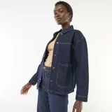 Campera vaquera azul oscuro con bolsillos de parche delanteros, cierre frontal de botones metálicos y costuras contrastantes en tono tostado.