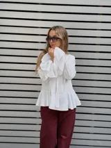 Blusa blanca de textura arrugada, con escote en V y lazos para anudar. Presenta mangas largas con puños acampanados y un diseño con volado en el ruedo.