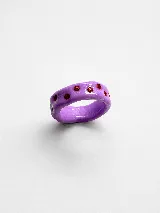 Anillo artesanal de arcilla polimérica en color lila, con diseño irregular y detalles de pequeñas piedras brillantes incrustadas en color rojo.