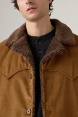 Campera corta de pana color marrón, con cuello y forro de borrego marrón oscuro. Tiene cierre frontal con botones y bolsillos laterales.