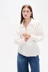Camisa blanca de algodón con diseño cruzado y anudado lateral, cuello camisero y mangas largas con puños.
