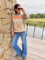 Sweater de punto en tono beige con diseño geométrico en colores naranja y blanco. Presenta cuello redondo, mangas largas y puños acanalados.