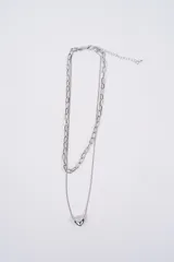 Collar doble de cadena plateada, compuesto por una cadena de eslabones gruesos y una cadena fina con un dije de corazón liso.