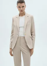 Chaqueta tipo blazer de corte entallado en color beige, con cuello de solapas con muesca, hombros estructurados, cierre frontal de un botón y bolsillos de ribete delanteros.