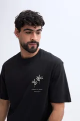 Remera oversize Brooksfield de color negro, confeccionada en 100% algodón, de manga corta y corte relajado. Cuenta con un diseño estampado en relieve en la espalda que representa flores abstractas y texto descriptivo en tono verde militar.