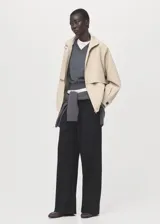 Chaqueta oversize de algodón color beige, con cuello alto, cierre frontal oculto con cremallera, mangas largas con puños abotonados, bolsillos laterales y bajo fruncido elástico.