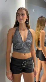 Short de tiro bajo confeccionado en material sintético con textura tipo cuero, color negro. Presenta una cintura ancha con una hebilla metálica rectangular decorativa en el centro.