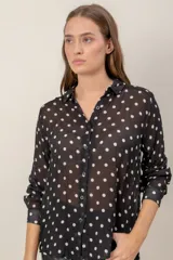 Camisa de tela semitransparente con estampado de lunares, cuello clásico, cierre frontal con botones y mangas largas con puños.