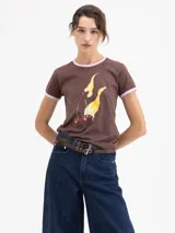 Remera de algodón pima orgánico color marrón, con cuello redondo y bordes de mangas en color rosa. Presenta un estampado frontal de cerezas con llamas.