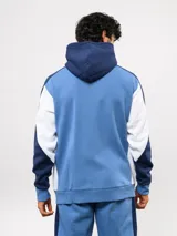 Campera deportiva Umbro del Club Nacional de Football, con cierre frontal, capucha ajustable con cordones y diseño en bloques de color azul, celeste y blanco. Presenta el logo de la marca y el escudo del club bordados en el pecho.