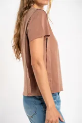 Remera de algodón color mostaza/naranja quemado, con cuello redondo y mangas cortas. Presenta un diseño con costuras externas visibles en los hombros y laterales, dándole un aspecto desestructurado.