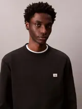 Buzo de algodón negro Calvin Klein, de cuello redondo, mangas largas y calce clásico. Presenta un pequeño parche con el monograma de la marca en el pecho y puños con ribete acanalado.