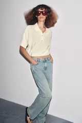 Polo de punto color crema, de manga corta y corte holgado, con cuello polo y tres botones frontales.