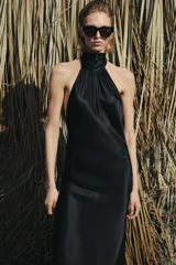 Vestido largo de satén negro con cuello halter subido y espalda descubierta. Presenta un diseño fluido con bajo en línea evasé.