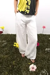 Pantalón de lino blanco de corte amplio y tiro medio-bajo. Presenta bolsillos laterales y traseros, cierre con botón metálico grabado y detalles de bordados laterales y traseros.