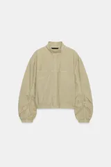 Cazadora de cuello subido con cierre frontal de botones a presión. Presenta mangas largas con detalle de frunces y puños elásticos, además de bajo elástico y bolsillos frontales.