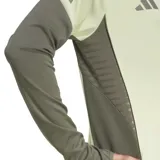 Buzo de entrenamiento Adidas del Real Madrid, color verde claro con mangas grises y detalles en gris oscuro. Presenta cuello alto con cierre de cremallera, logo de Adidas y escudo del Real Madrid en el pecho.